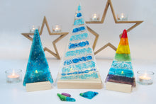 Load image into Gallery viewer, Three brightly coloured Christmas Tree tealights are displayed with star shaped Christmas decorations, other tealights and glass pebbles